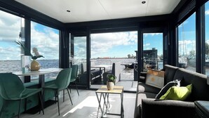 Un intérieur moderne comprenant un coin repas, des sièges et de grandes fenêtres offrant une vue sur l’eau.