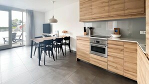 Een moderne keuken met houten kastjes, een inbouwoven en een eethoek met een tafel en stoelen.