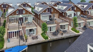 Een rij moderne huizen met grote ramen, een houten terras en uitzicht op een kanaal.