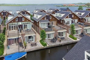 Een rij moderne huizen met grote ramen, een houten terras en uitzicht op een kanaal.
