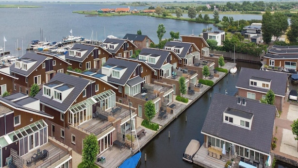 Een woongebied aan een gracht met moderne huizen, een steiger en boten.