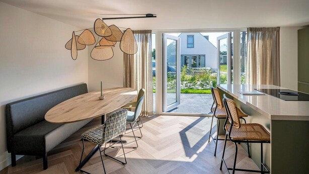 A modern living room with a round table, two chairs, a sofa, and a large window with a view of a house and greenery. - 6-Guest Holiday Home with Terrace (Sint Maarten)