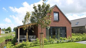 A modern house with a brick exterior, a covered patio with outdoor furniture, and a small garden area. - 6-Guest Holiday Home with Terrace (Sint Maarten)