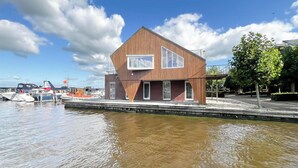A modern building with a triangular roof, a large window, and a waterfront view. - Penthouse with Lake View Terrace (Uitgeest)