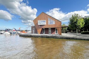 A modern building with a triangular roof, a large window, and a waterfront view. - Penthouse with Lake View Terrace (Uitgeest)