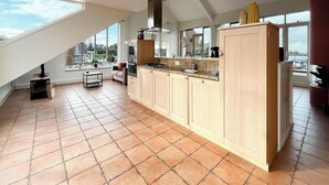 A modern kitchen with a large island, a built-in oven, and a large window providing a view of the outdoors. - Penthouse with Lake View Terrace (Uitgeest)