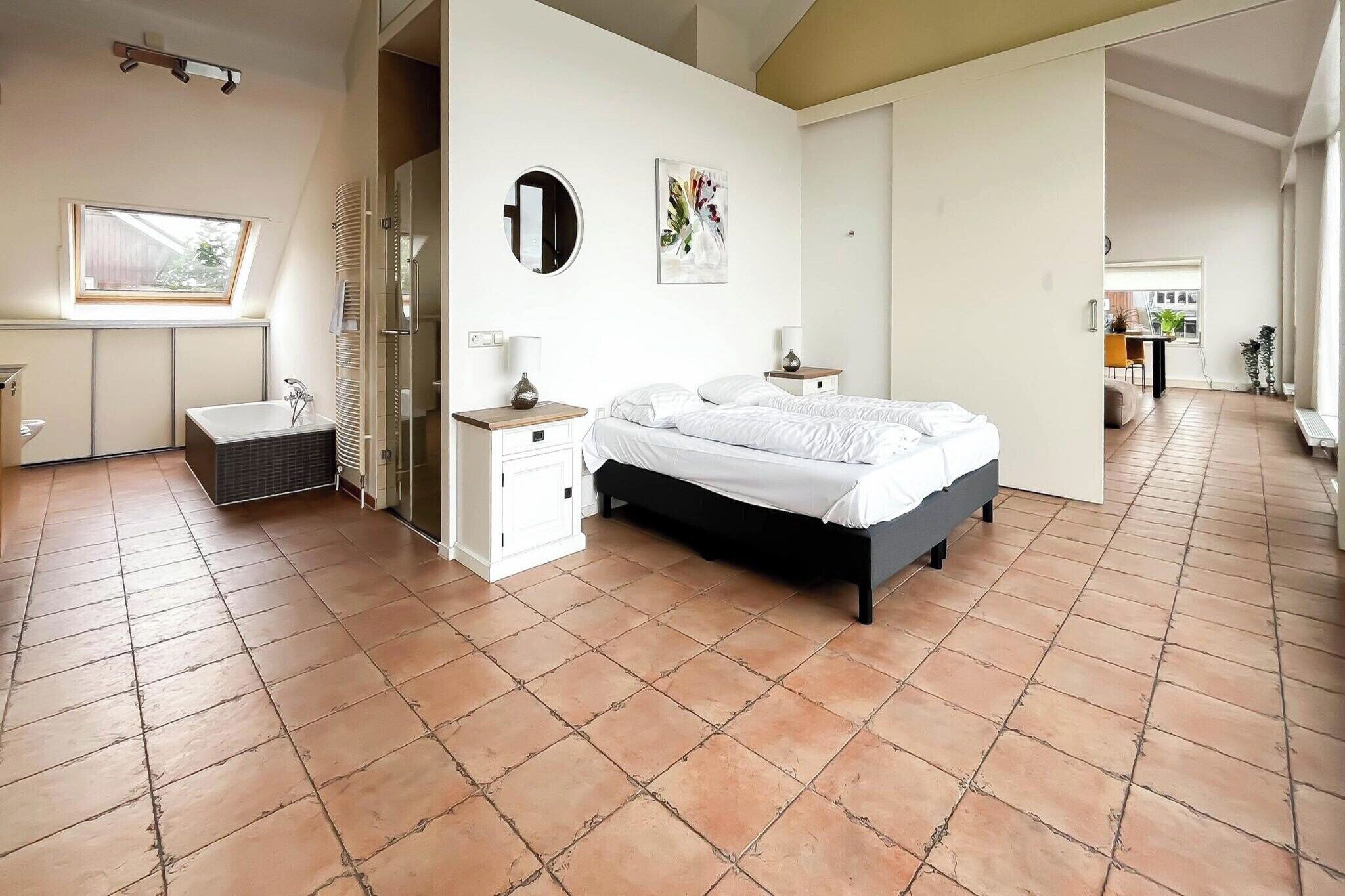Une chambre à coucher comprenant un lit, une table de chevet, un miroir, une fenêtre, ainsi qu’une salle de bain avec une baignoire et des toilettes.