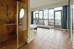 A hotel room with a large window, a bed, a shower area, and a view of a dock with boats. - Penthouse with Lake View Terrace (Uitgeest)