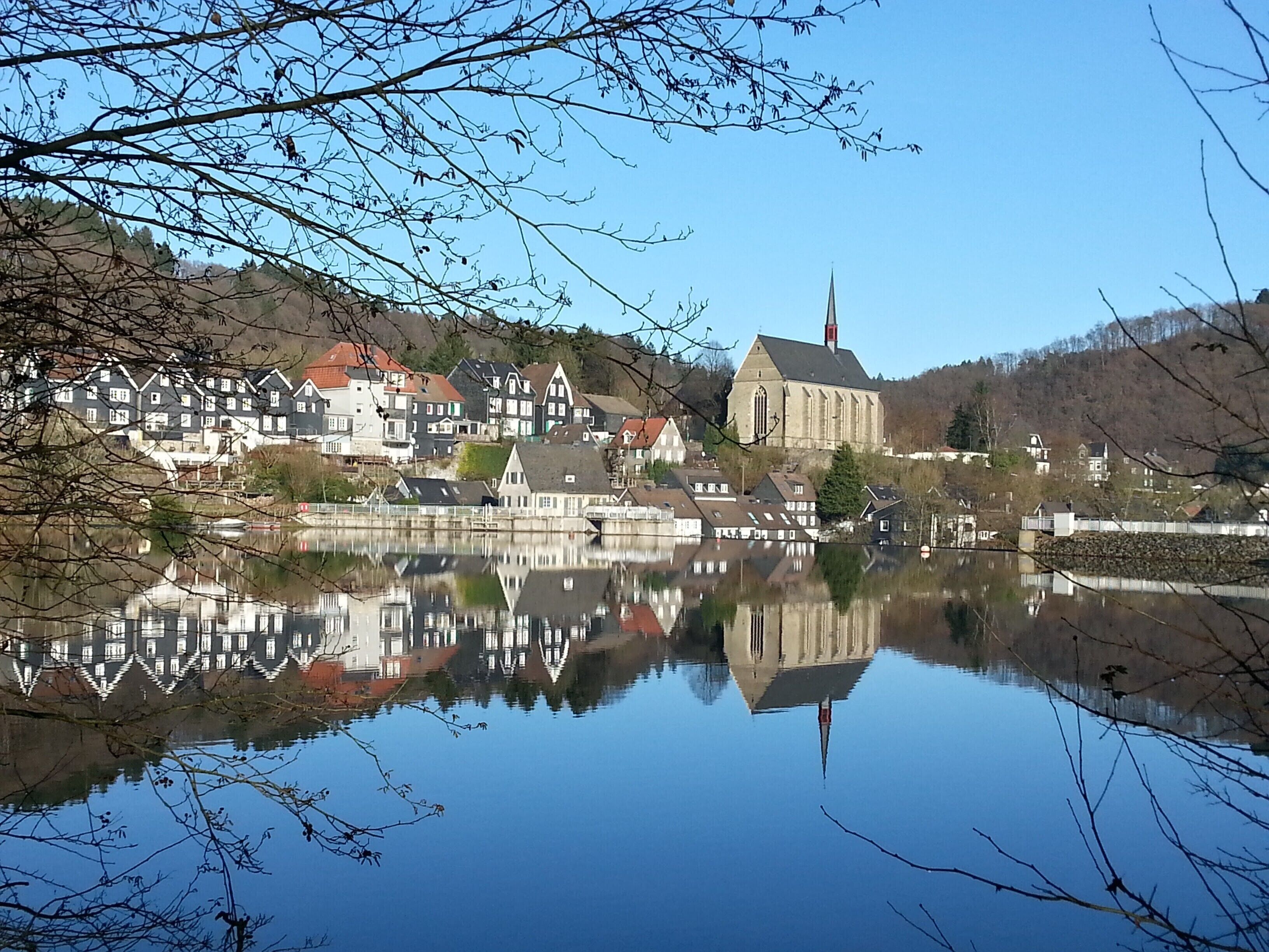Un llac tranquil que reflecteix edificis, incloent-hi una església amb un campanar alt.