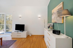 A modern living room with a flat-screen TV, a white cabinet, a lamp, and a painting on the wall.