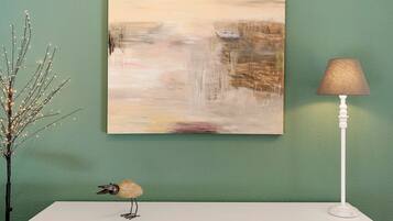 Un tableau, une lampe et une branche décorative posés sur une surface blanche, le tout sur fond de mur vert.
