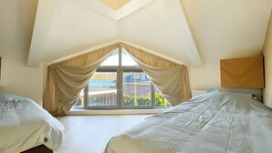 Ett sovrum med två sängar, ett stort fönster med gardiner och utsikt över omgivningen.