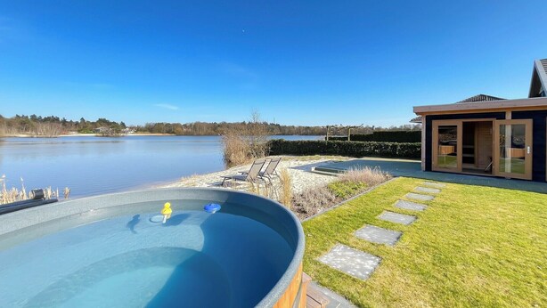 En swimmingpool med ett bubbelbad, en gräsyta och en modern byggnad med stora fönster.