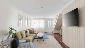 Ein Wohnzimmer mit einer Couch, einem runden Couchtisch, einem Flachbildfernseher und einer Treppe, die in einen oberen Bereich führt.