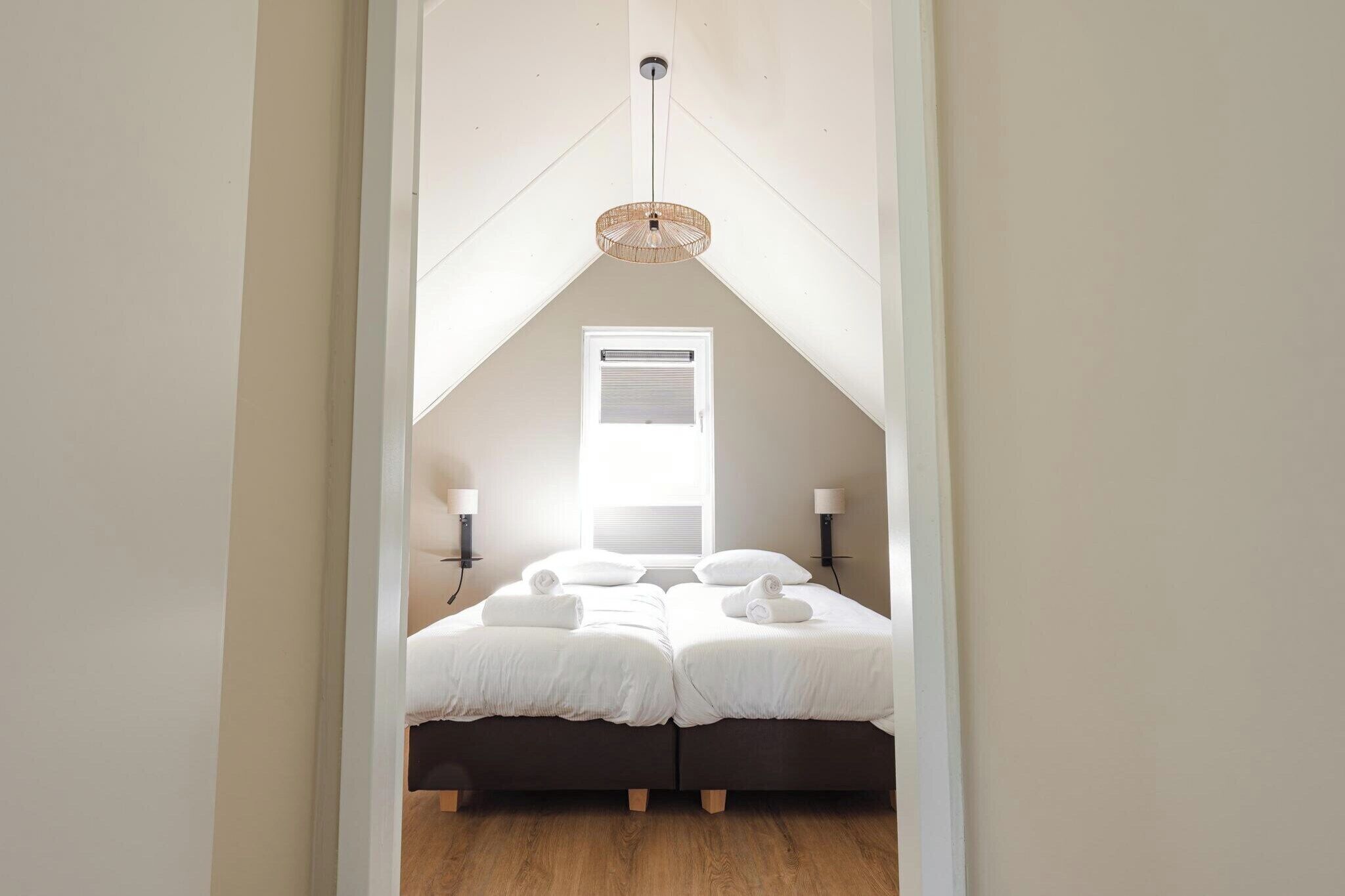 A bedroom with two beds, a window, a hanging light fixture, and wall-mounted lamps.
