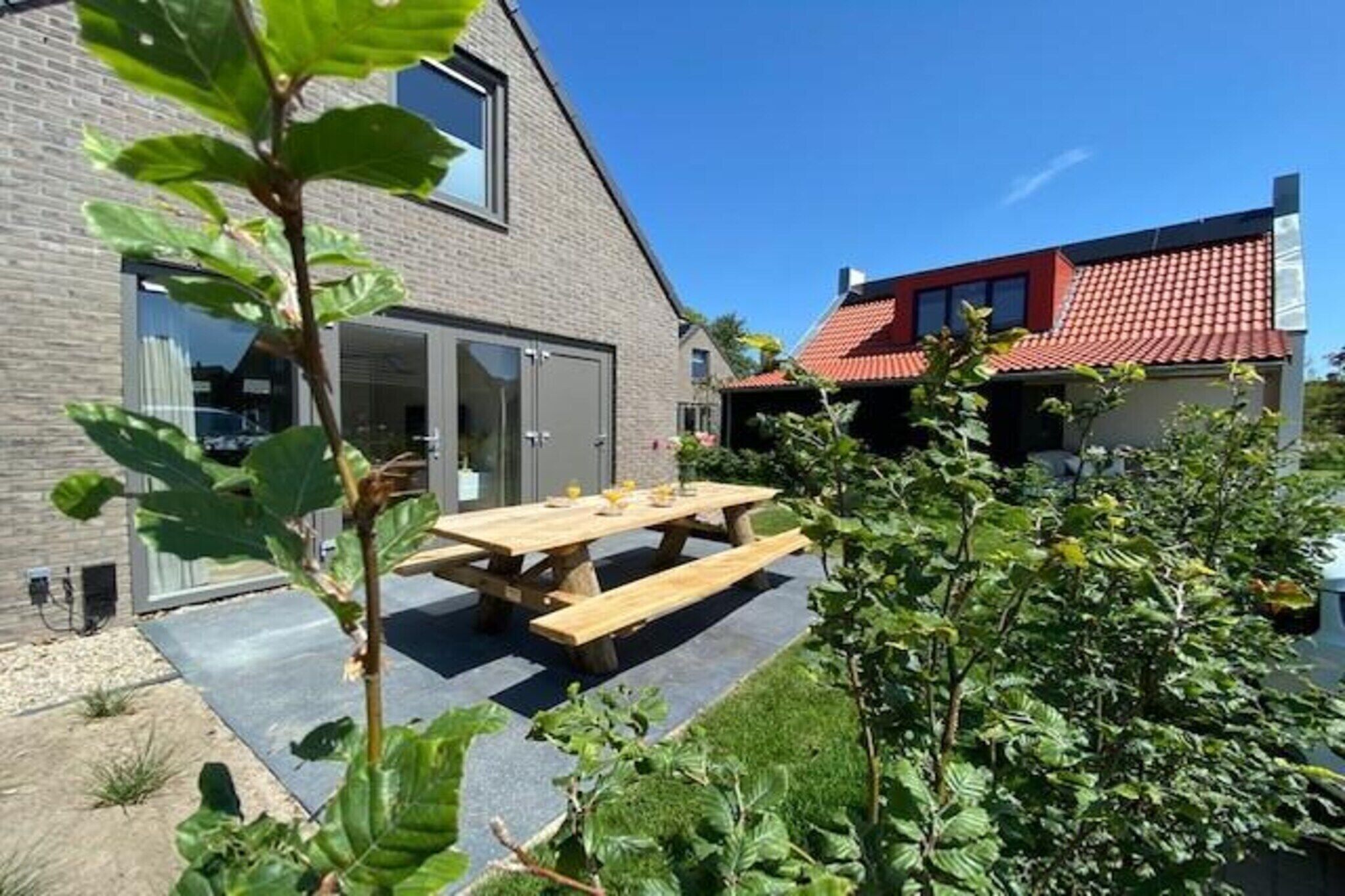 Ein Haus mit geneigtem Dach, einer Holzterrasse und einem Garten.