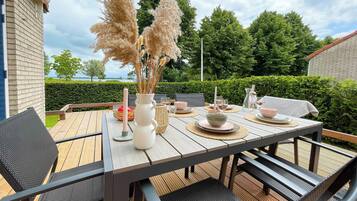 A wooden deck with a table set for dining, surrounded by greenery and a hedge.