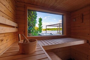 A wooden sauna with a window, a wooden bucket, and a bench. - Water Villa, Sauna & Beach (Sibculo)