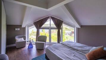 Een slaapkamer met een groot raam, een bed, een stoel en een klein tafeltje.