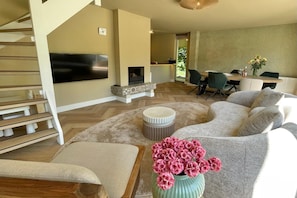 A modern living room with a fireplace, a dining area, and a staircase.