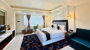 A hotel room with a large bed, a TV, a desk, a chair, and a sofa. - Hotel KAMA (Danapur)