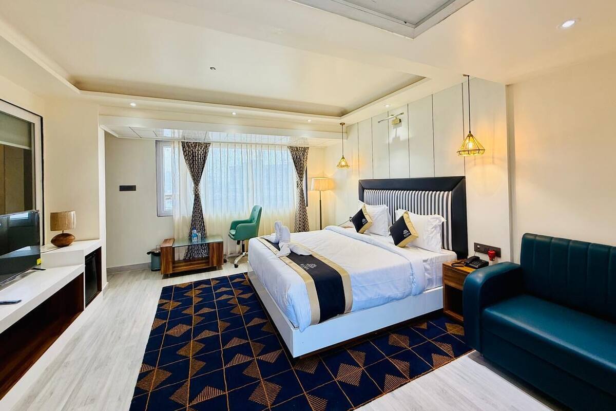 A hotel room with a large bed, a TV, a desk, a chair, and a sofa.