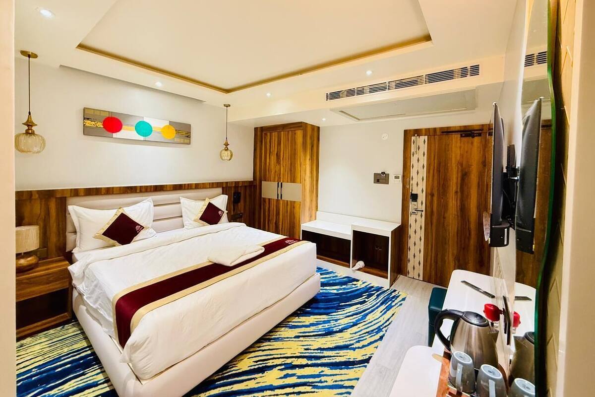 A hotel room with a bed, bedside tables, a desk, a chair, a TV, and a window.
