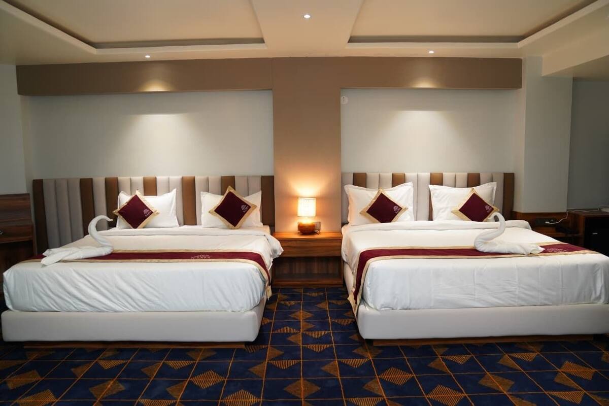 A hotel room with two beds, a nightstand with a lamp, and a patterned carpet.