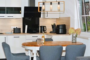 Ett modernt kök med en matplats, inklusive en kaffebryggare, vattenkokare och en flaska på bänkskivan.