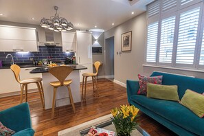 A modern kitchen with a central island, wooden chairs, a teal sofa, and a window with blinds. - Stylish London Retreat in Iconic Notting Hill (London)