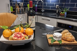 A kitchen counter with a bottle of wine, a bowl of fruit, a knife, and a croissant. - Stylish London Retreat in Iconic Notting Hill (London)