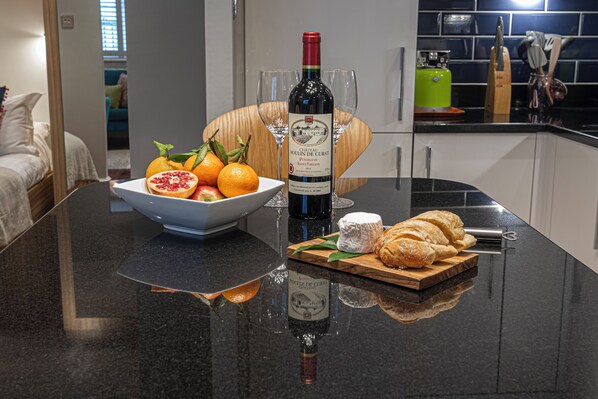 A kitchen counter with a bottle of wine, two glasses, a bowl of fruit, and a wooden board with pastries. - Stylish London Retreat in Iconic Notting Hill (London)