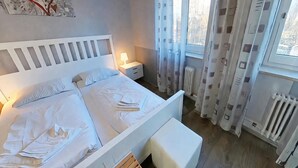 Ein Schlafzimmer mit Bett, Nachttisch, Lampe, Vorhängen und Heizkörper.