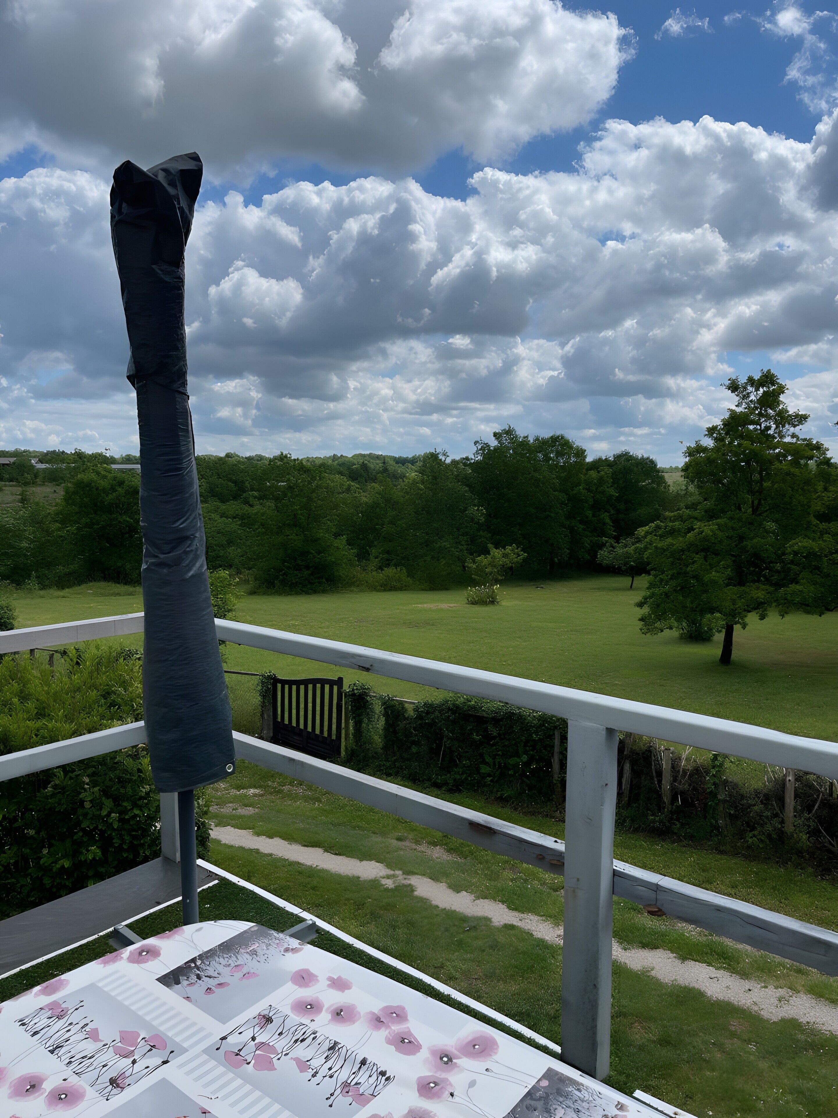 Uma varanda com vista para um campo gramado e árvores sob um céu parcialmente nublado.