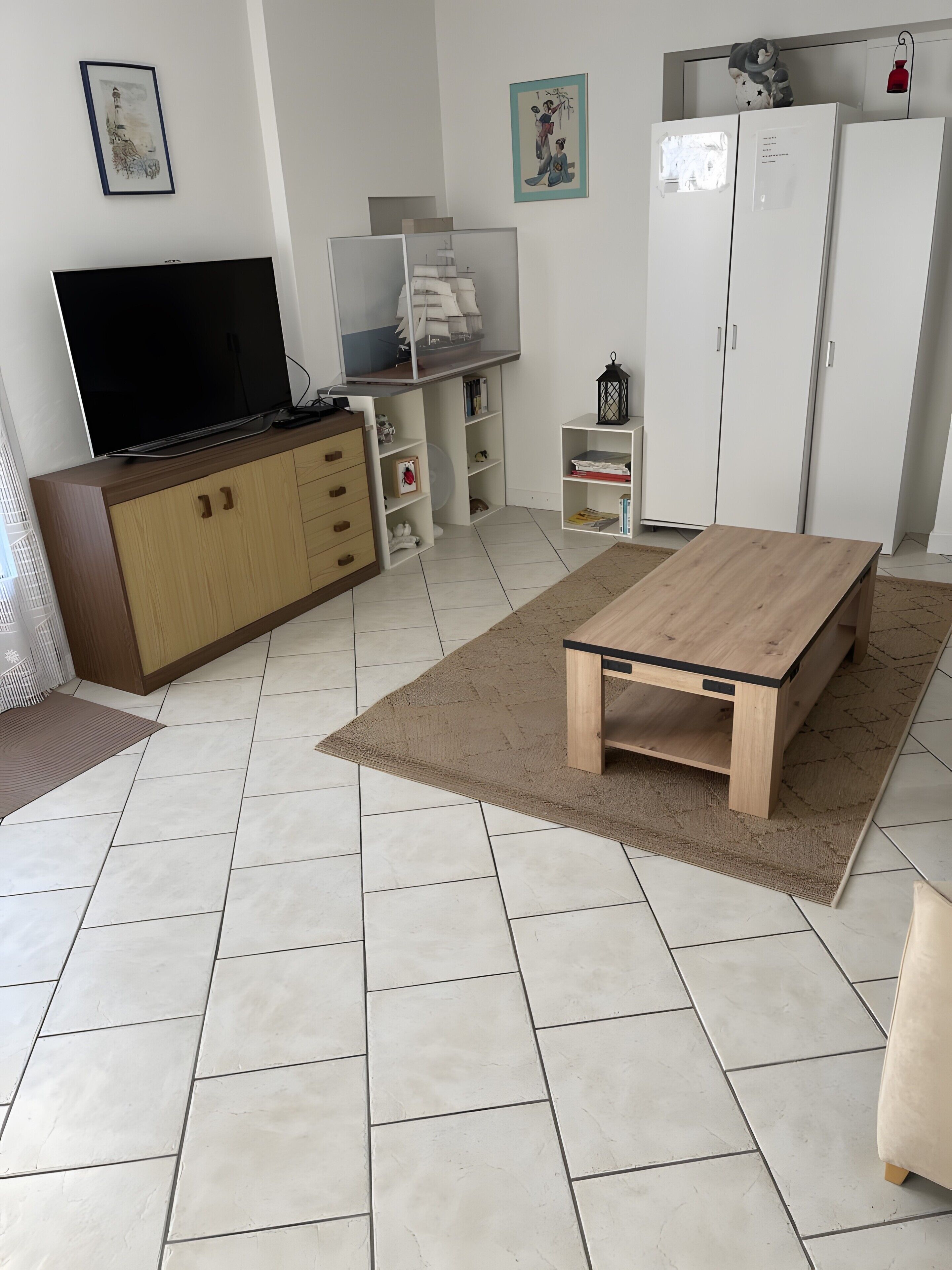 Sala de estar con televisor, mueble de madera, estanterías, una mesita y un refrigerador.