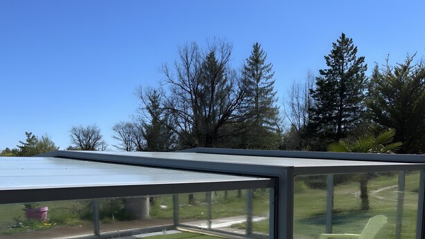 A swimming pool with a glass enclosure, surrounded by a wooden deck and a grassy area with trees.