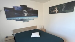 A bedroom with a bed, a nightstand, a lamp, and wall art depicting space and a tiger.
