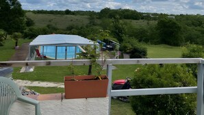 A balcony with a view of a swimming pool, a covered patio area, and a lush green landscape.