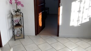A room with a tiled floor, a wooden door, a potted orchid, a small table, and a sofa with a floral cushion.