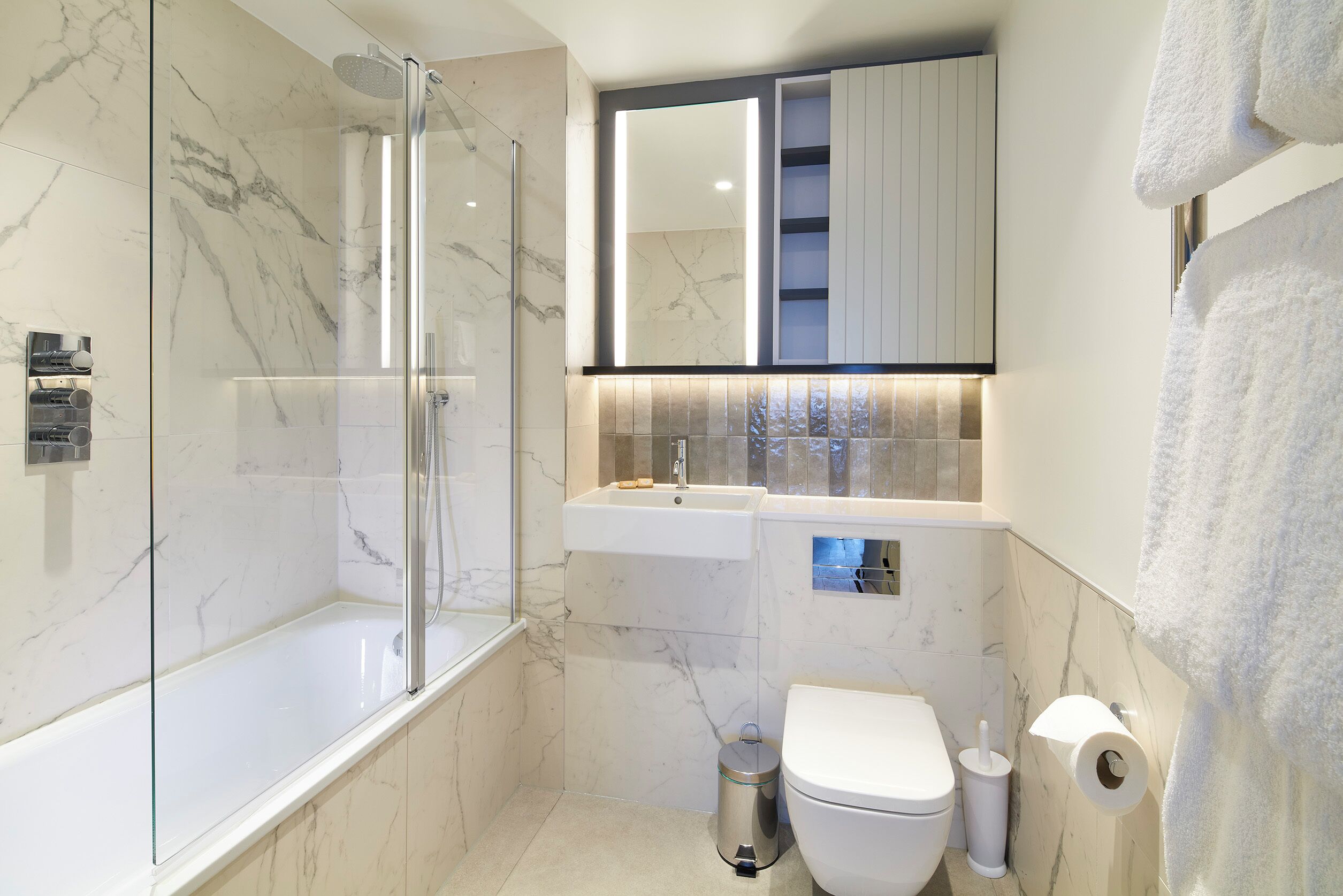 A modern bathroom with a glass-enclosed shower, a white toilet, and a sink with a mirror above.