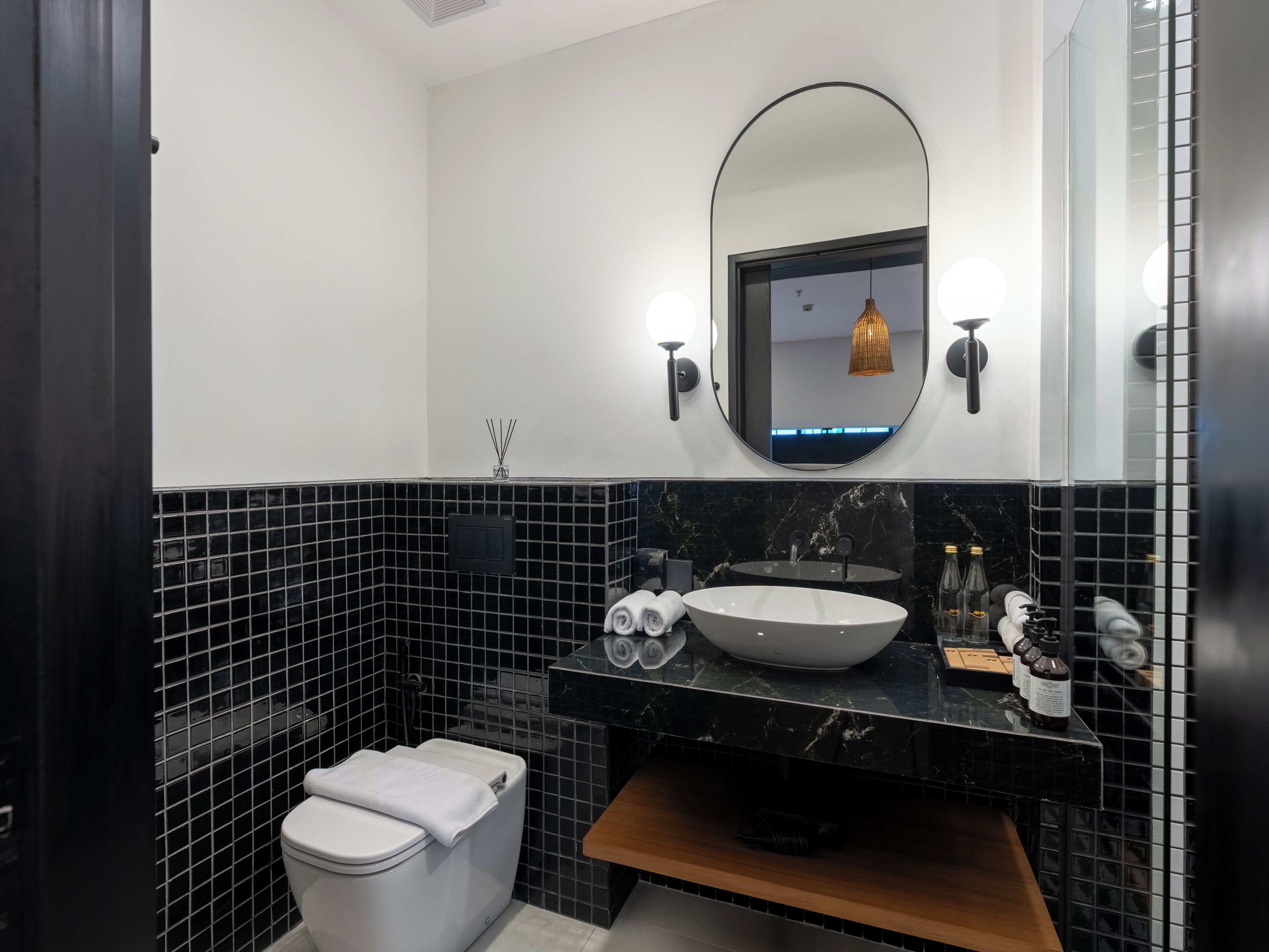 A modern bathroom with a white toilet, black tiled walls, a round mirror, and a vessel sink.