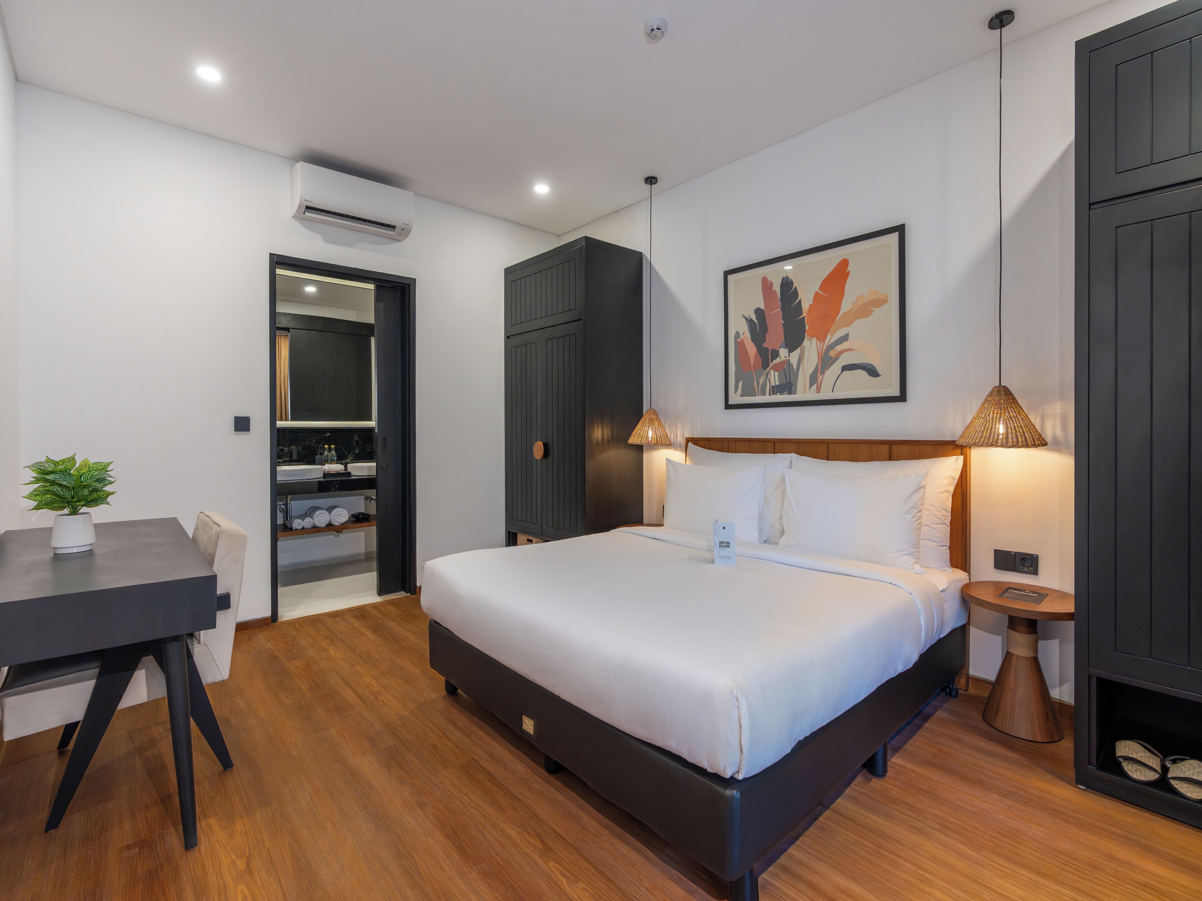 A modern hotel room with a bed, bedside tables, a desk, and a bathroom visible through an open door.