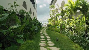 A pathway flanked by lush greenery and white buildings with arched windows and balconies.