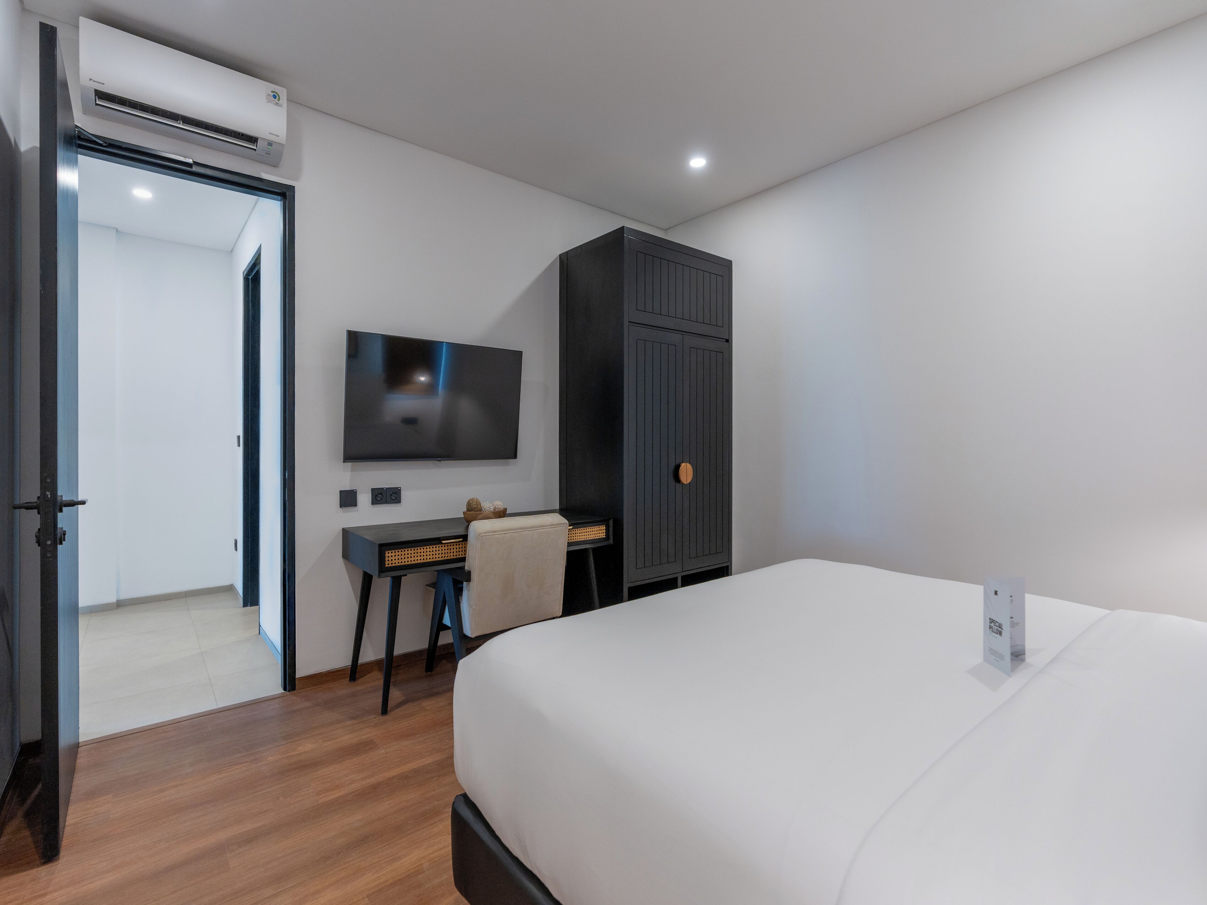 A modern hotel room with a large bed, a desk with a chair, a television, and a wardrobe.