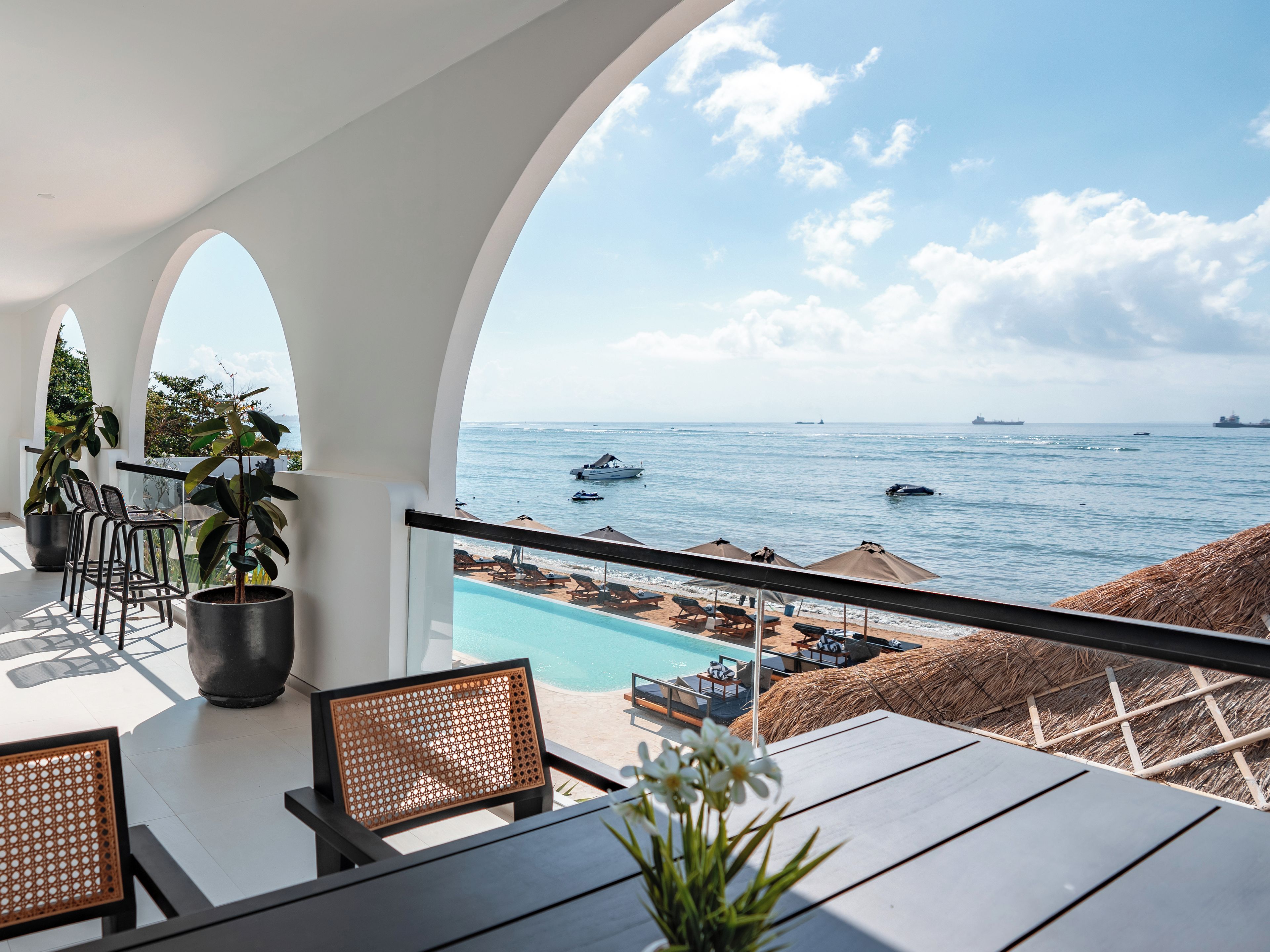 A balcony with a view of the sea, lounge chairs, and a pool.