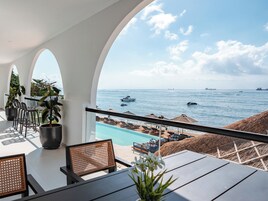 A balcony with a view of the sea, lounge chairs, and a pool.