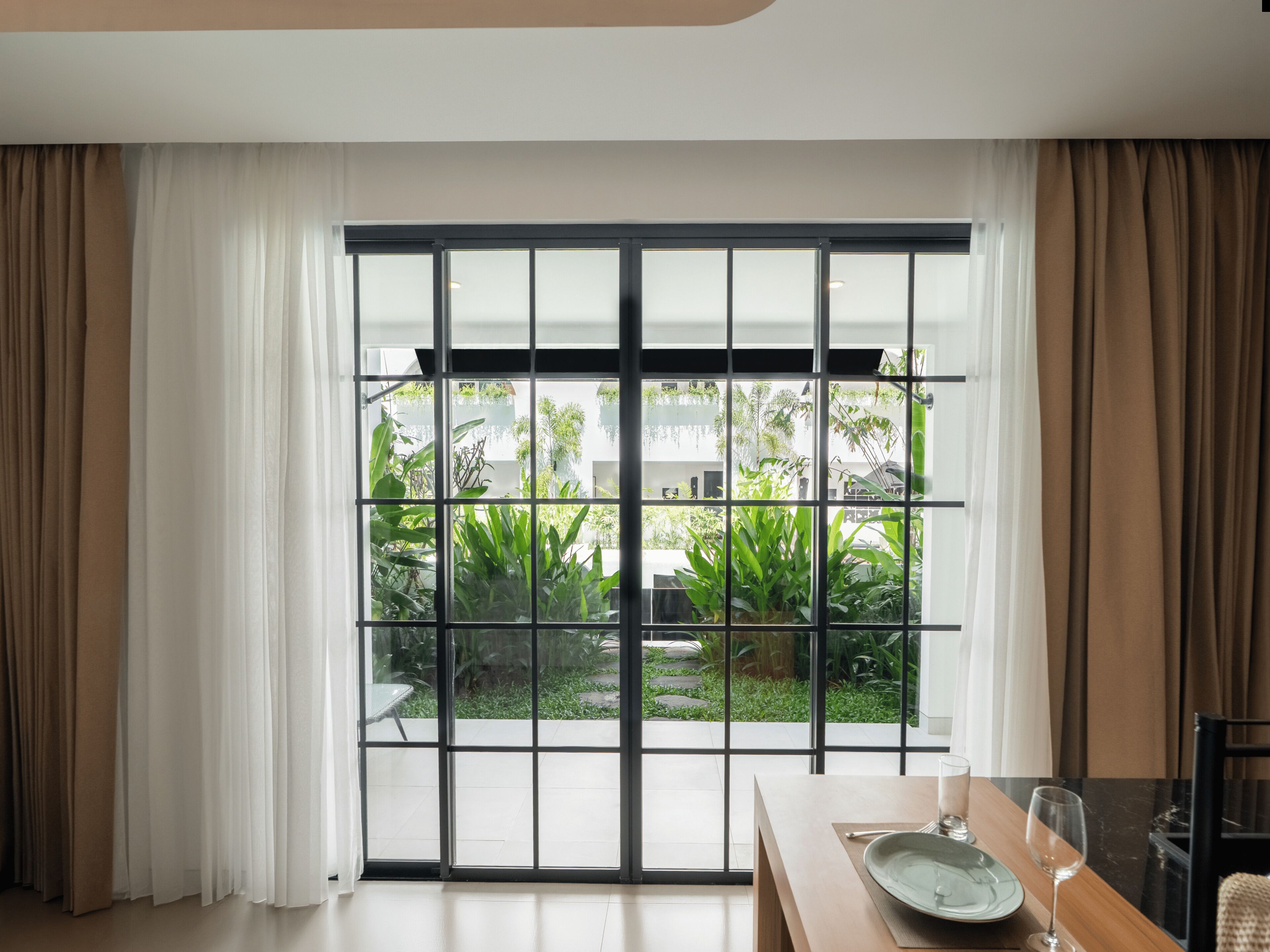 A room with a large sliding glass door leading to a garden, a dining table with a plate and glass, and a chair.