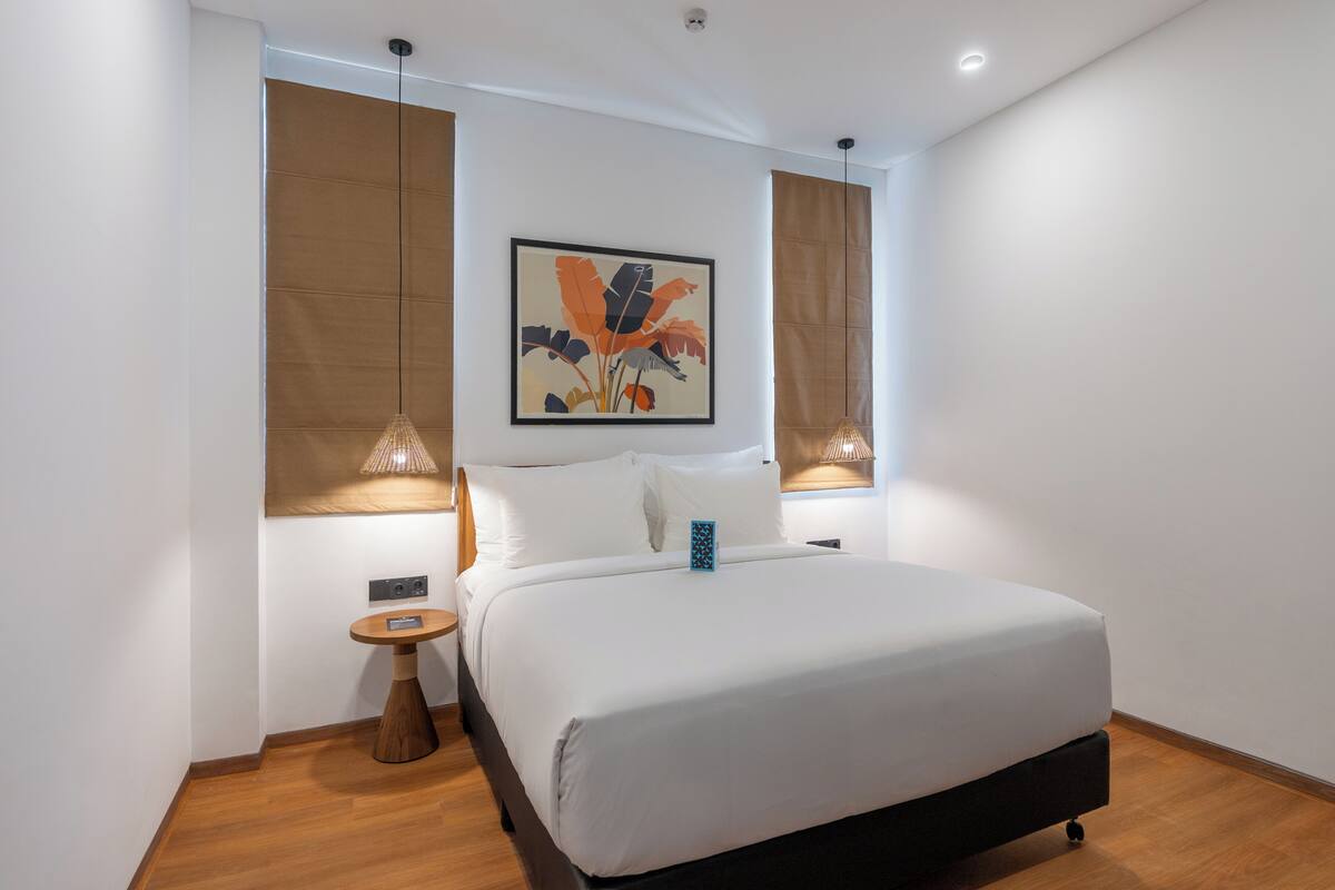 Ein modernes Hotelzimmer mit einem großen Bett, einem kleinen Nachttisch, einem Wandbild und einem Fenster mit Vorhängen.