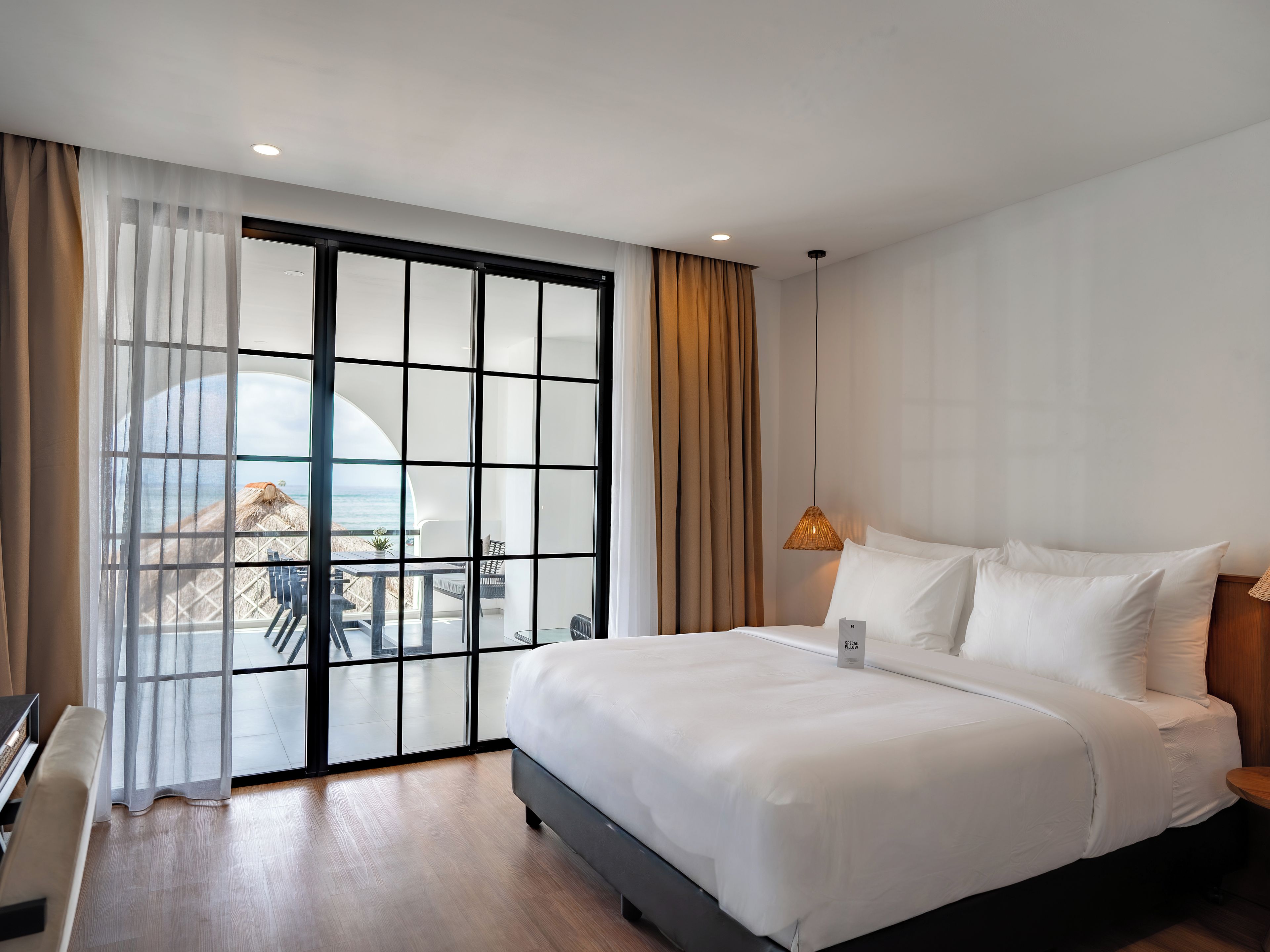 Een hotelkamer met een groot bed, uitzicht op het strand door een glazen deur en een balkon met tuinmeubilair.