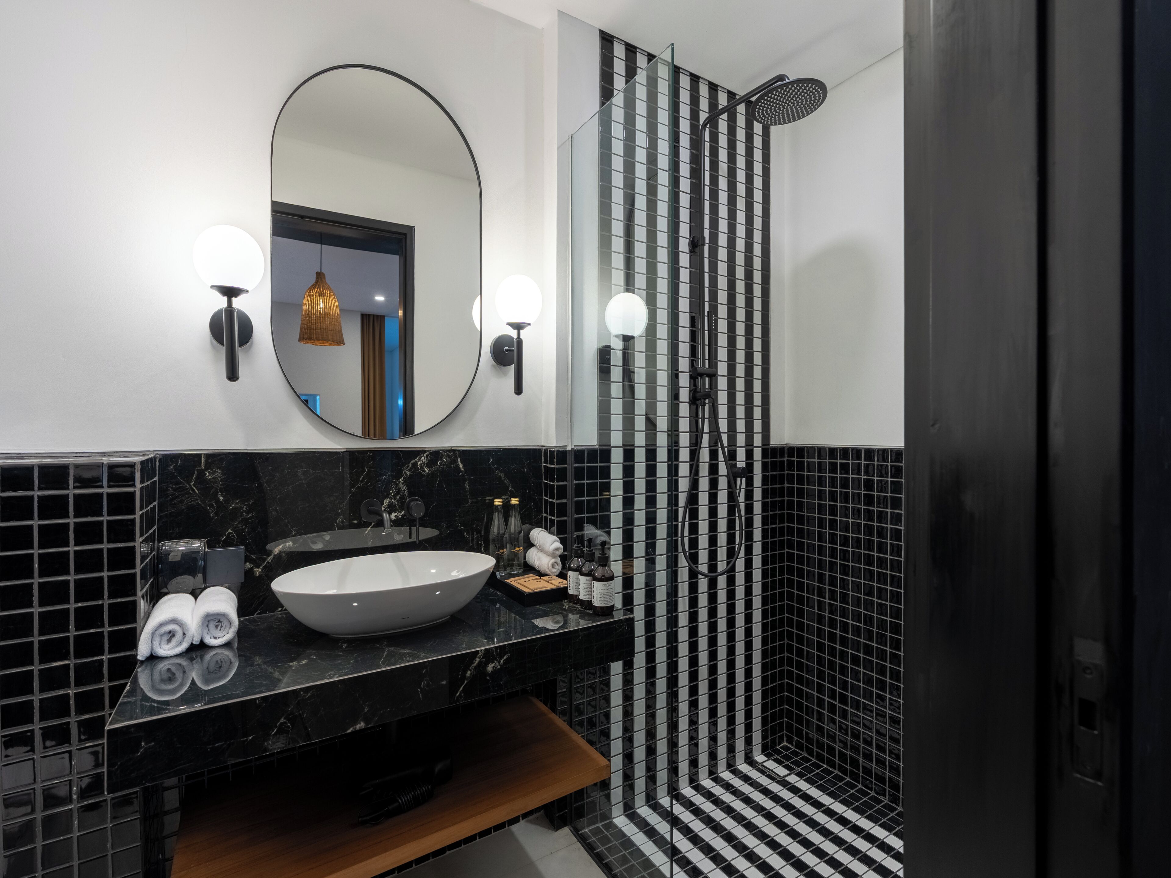 A modern bathroom with a large oval mirror, a round sink, and a black and white checkered shower area.